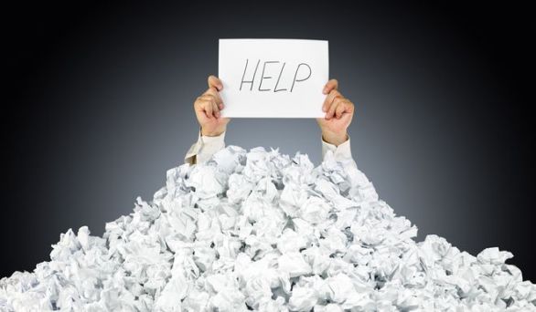 Person under crumpled pile of papers with hand holding a help si